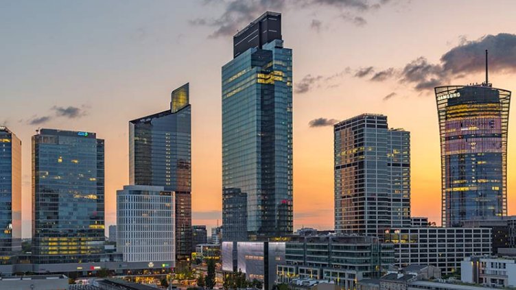 The skyline of a city at sunset, featuring towering buildings outlined by a colorful sky of orange and purple hues.