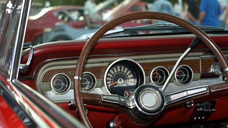 View from classic red convertible through windshield at a car show
