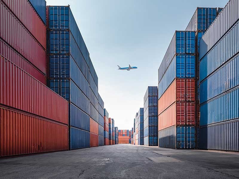 An airplane above a port with containers