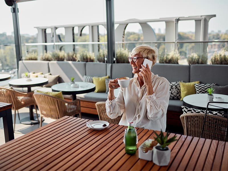 A woman sitting on a chair in a hotel and having a cup of tea, smiling while talking on phone