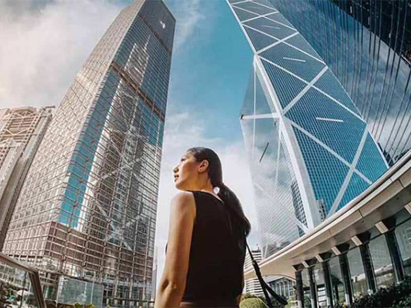 A female standing on the road and looking towards various real estate buildings surrounding her