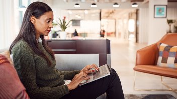 Businesswoman Sitting On Sofa Working On Laptop At Desk In Shared Workspace Office