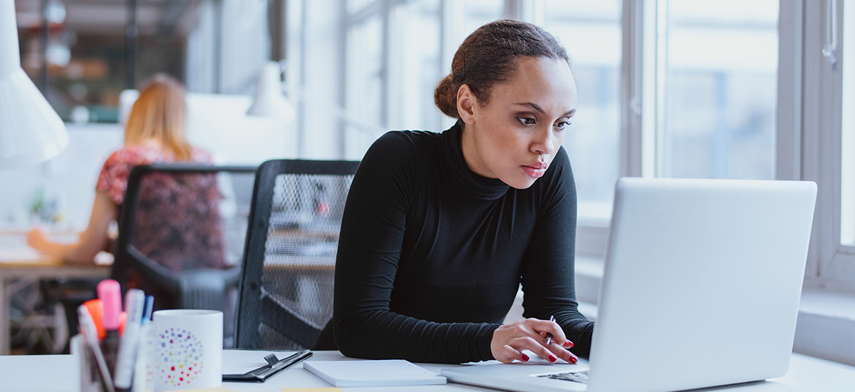 Picture of a professional lady working on her laptop sitting at the workspace inside the office